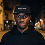 Person wearing a black hoodie and cap with 'MAGDALENA' text, standing on a street at night.