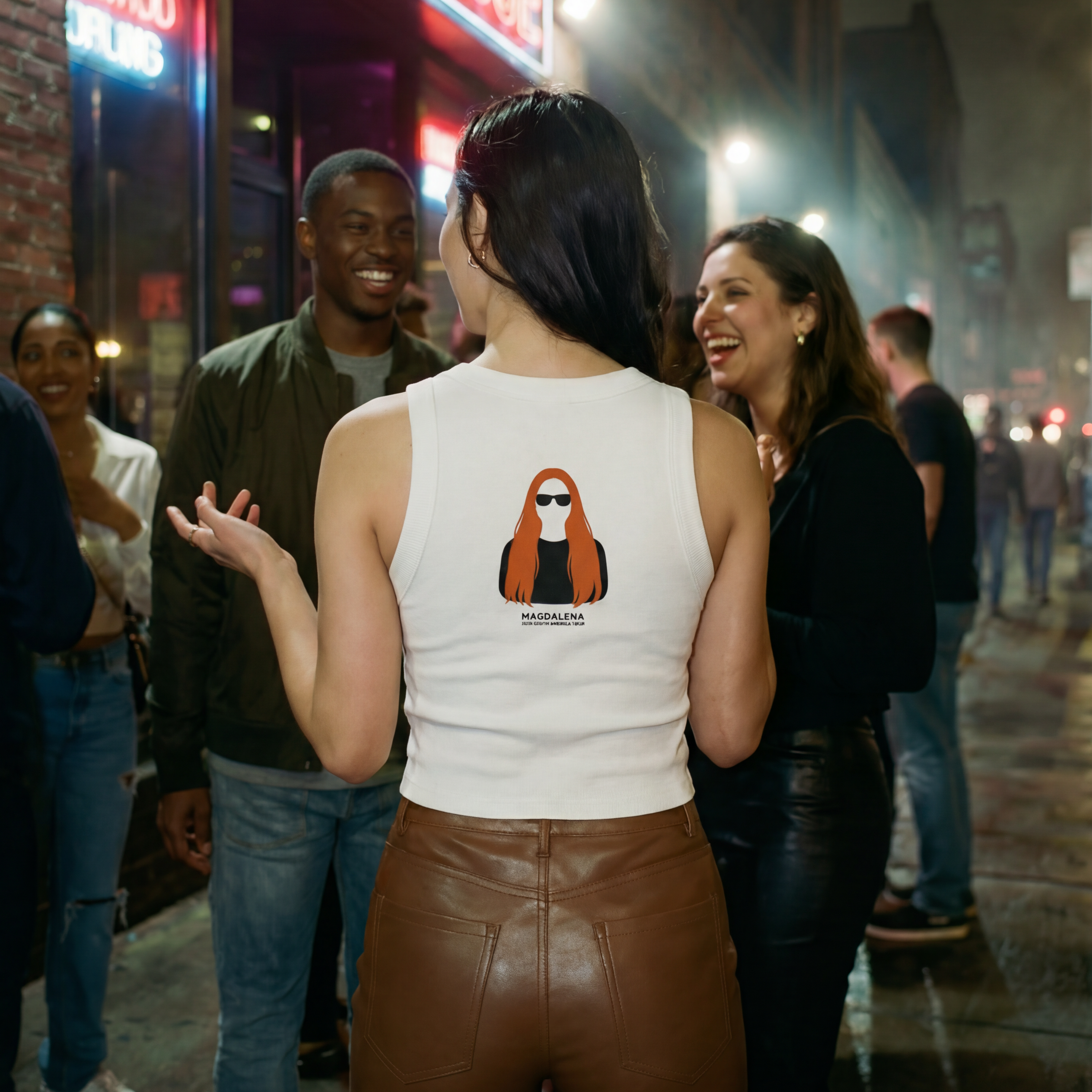 Woman in a white tank top with a Magdalena graphic design on the back, standing in a lively street scene at night.