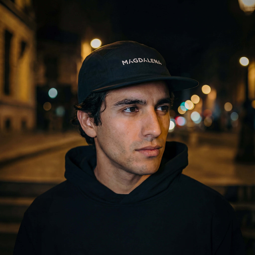 Man wearing a black cap with 'Magdalena' text in an urban night setting