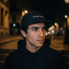 Man wearing a black cap with 'Magdalena' text in an urban night setting