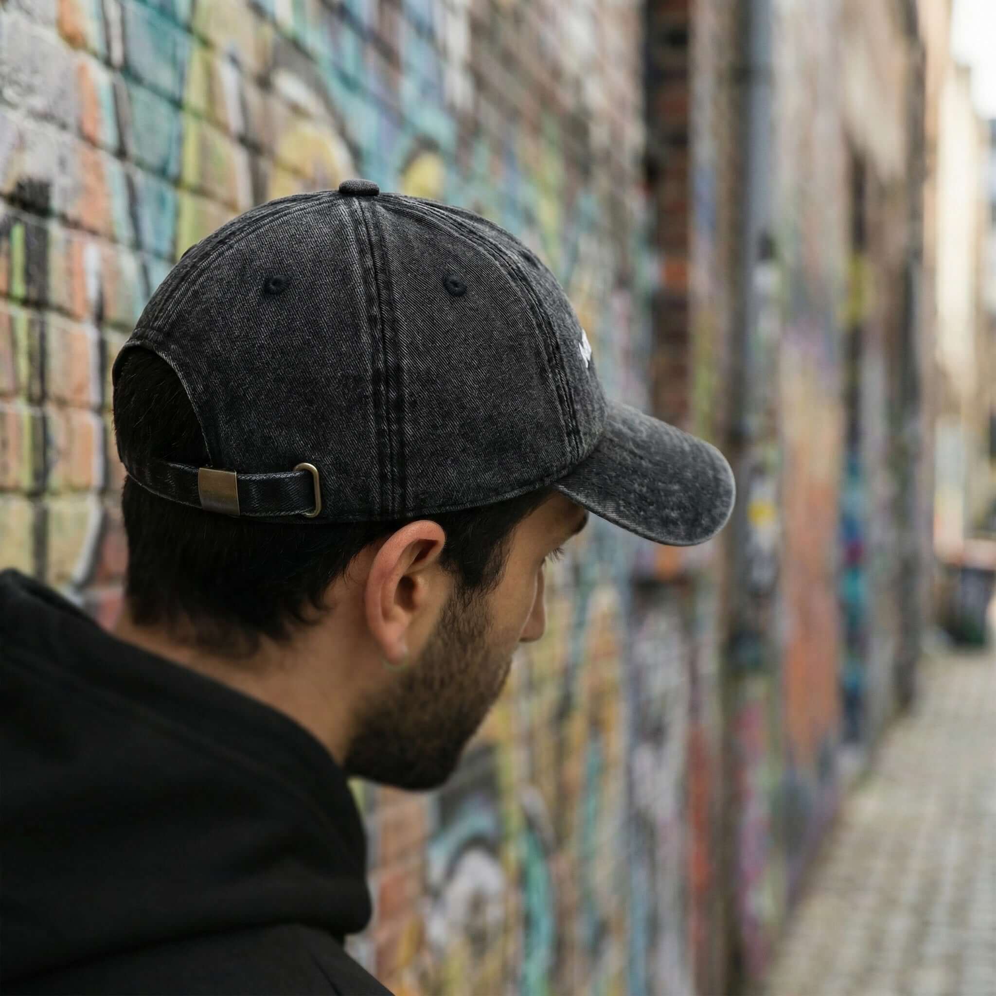 Person wearing a 'MAGDALENA' black cap and hoodie in front of a graffiti-covered wall